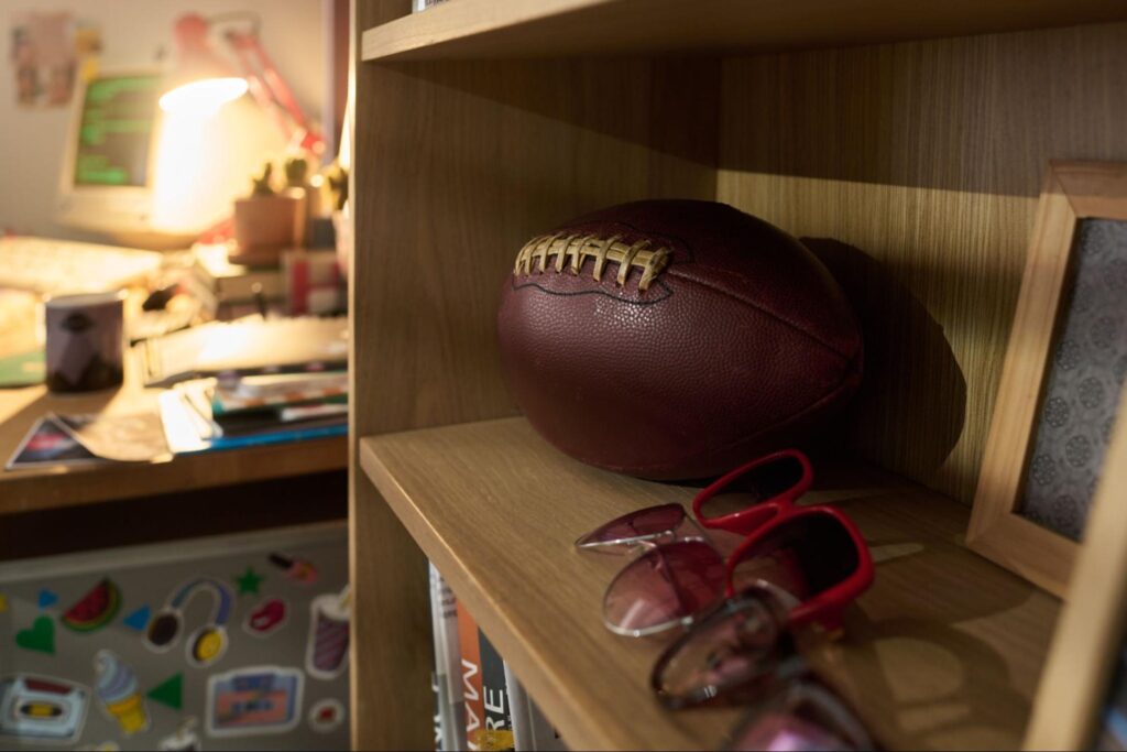 Football and stylish sunglasses displayed on a wooden shelf in a cozy room.