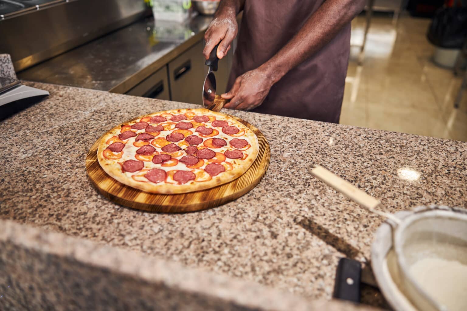 Pizzaiolo cutting fresh pepperoni pizza at a bustling pizzeria counter.