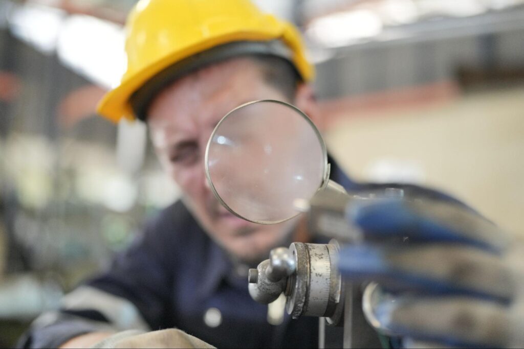 Worker using precision tools to inspect details in a manufacturing setting.