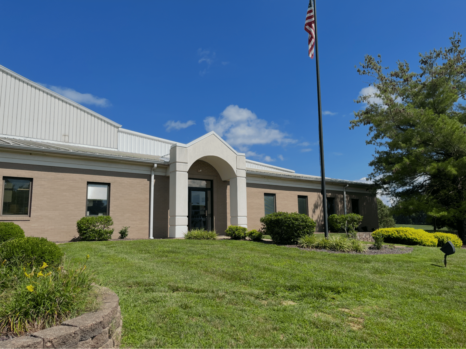 Modern building with flag and greenery under a clear blue sky.