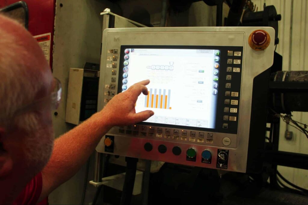 Operator using touchscreen to monitor custom injection molding machine performance metrics and efficiency.